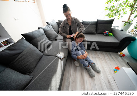 Tender moments shared between a mother and daughter as hair is styled in their cozy living room filled with warmth and love during a sunny afternoon 127446180