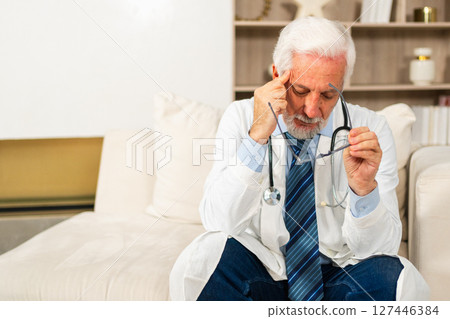 Sad tired mature senior male doctor in medical uniform in hospital or doctor office. Unhappy General Practitioner GP therapist professional healthcare expert in clinic. Healthcare concept 127446384