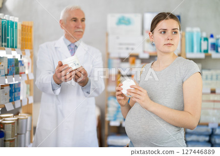 Pregnant girl looking for skin cream in a pharmacy. Male pharmacist helps to choose right skin cream 127446889