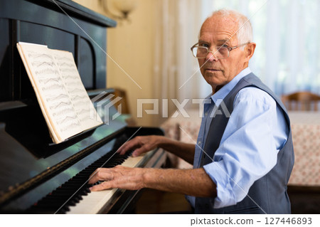 Old man playing piano at home 127446893