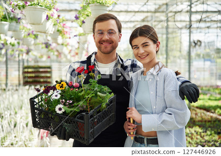 Sincere smile, standing, holding flowers. Man and woman are together in bright greenhouse 127446926