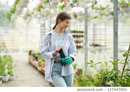 Florist woman is standing. Successful employee is in a bright greenhouse Florist woman is standing. Successful employee is in a bright greenhouse 127447003