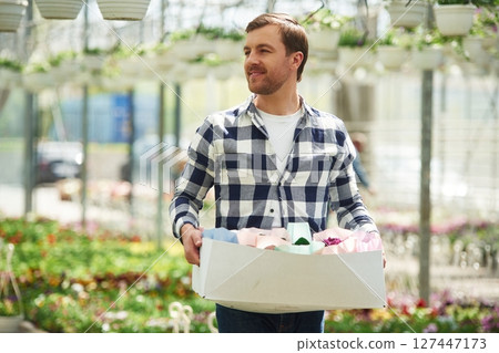 With paper box with stuff. Florist man working in garden center. Successful employee is in a bright greenhouse With paper box with stuff. Florist man working in garden center. Successful employee is in a bright greenhouse 127447173