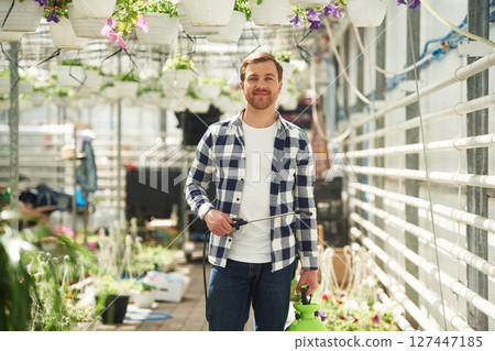 Positive florist man is working in garden center. Successful employee is in a bright greenhouse Positive florist man is working in garden center. Successful employee is in a bright greenhouse 127447185