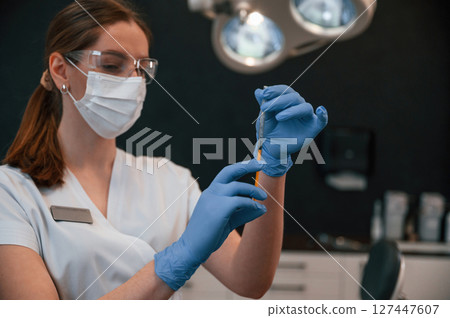 Doctor in blue glowes is standing and holding equipment. In the stomatological cabinet Doctor in blue glowes is standing and holding equipment. In the stomatological cabinet 127447607