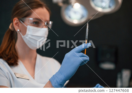 Doctor in blue glowes is standing and holding equipment. In the stomatological cabinet Doctor in blue glowes is standing and holding equipment. In the stomatological cabinet 127447608
