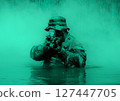 Soldier in a camouflage uniform and hat aiming a rifle while half-submerged in water, with a background of green mist. 127447705