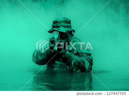 Soldier in a camouflage uniform and hat aiming a rifle while half-submerged in water, with a background of green mist. 127447705