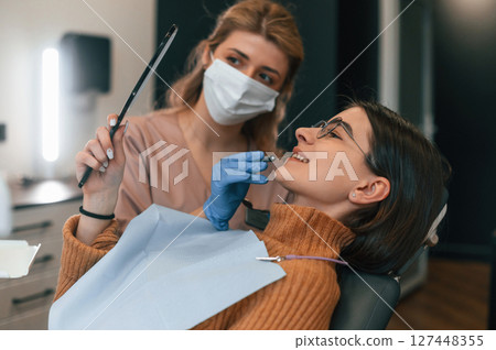 Woman is looking at her teeth in the mirror. In the stomatological cabinet 127448355
