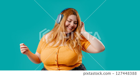 Overweight pretty woman gets high,listening music with headphones on blue studio Overweight pretty woman gets high,listening music with headphones on blue studio 127448388