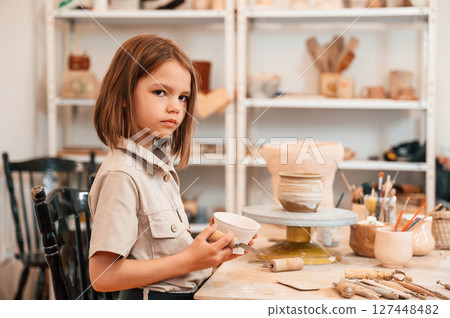 Little girl is indoors with ceramic pot in hands 127448482