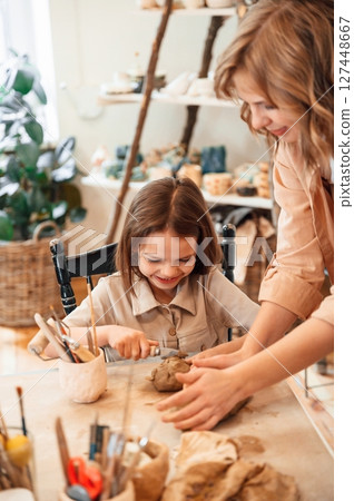 Creating the shape by using clay. Mother with little girl doing pottery at home Creating the shape by using clay. Mother with little girl doing pottery at home 127448667