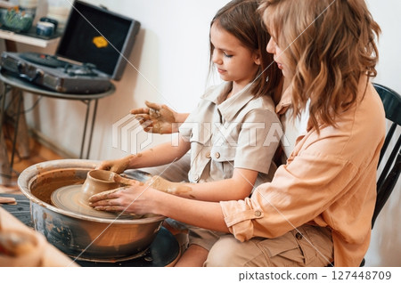 Sitting, creating the shape. Mother with little girl doing pottery at home 127448709