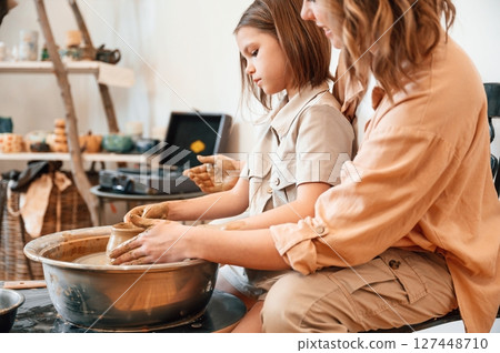 Sitting, creating the shape. Mother with little girl doing pottery at home 127448710