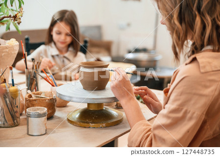 Painting the product. Mother with little girl making ceramic pot at home Painting the product. Mother with little girl making ceramic pot at home 127448735