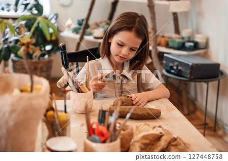 Working with clay. Little girl is learning how to do pottery in the workshop 127448758