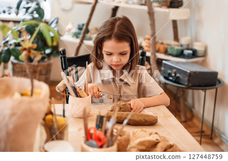 Working with clay. Little girl is learning how to do pottery in the workshop 127448759