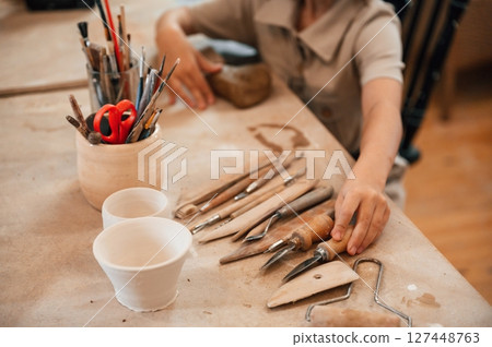Different tools on the table. Little girl is learning how to do pottery in the workshop Different tools on the table. Little girl is learning how to do pottery in the workshop 127448763