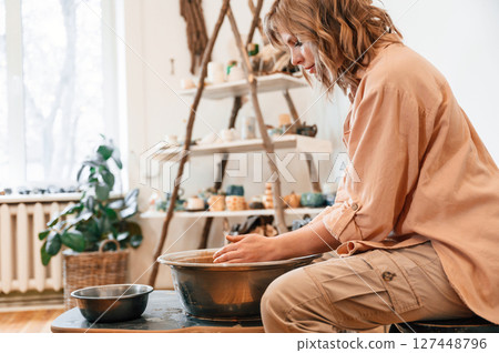Woman is sitting and creating a handmade ceramic bowl in a pottery Woman is sitting and creating a handmade ceramic bowl in a pottery 127448796