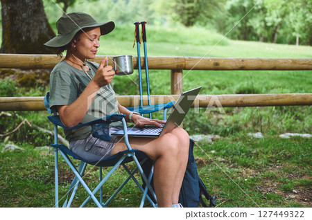 Woman Working on Laptop Outdoors While Sipping Coffee in Nature 127449322