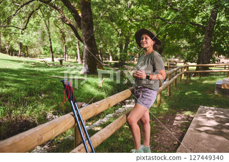Woman Enjoying a Refreshing Drink in a Green Park While Hiking Woman Enjoying a Refreshing Drink in a Green Park While Hiking 127449340