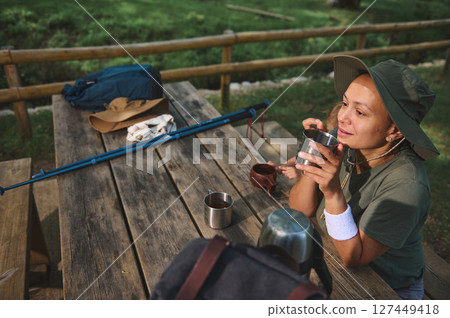 Woman Enjoys a Relaxing Outdoor Break at a Rustic Picnic Table in a Scenic Natural Setting Woman Enjoys a Relaxing Outdoor Break at a Rustic Picnic Table in a Scenic Natural Setting 127449418