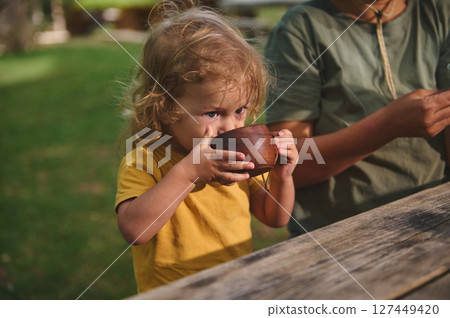 Young Child Drinking Outdoors With Family at a Rustic Table Young Child Drinking Outdoors With Family at a Rustic Table 127449420