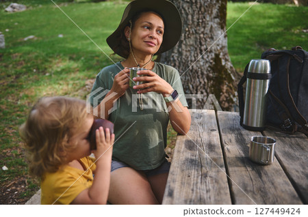 Mother and Child Enjoying Time Outdoors With Beverages in Green Nature Mother and Child Enjoying Time Outdoors With Beverages in Green Nature 127449424