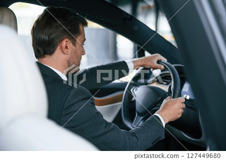 Rear view. Businessman in suit is driving his electric car Rear view. Businessman in suit is driving his electric car 127449680