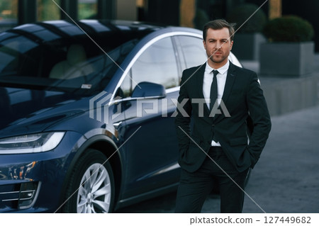 Standing, in black suit. Businessman is near his car outdoors 127449682