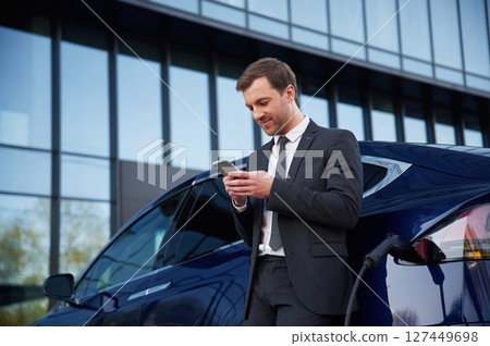 Using smartphone. Businessman is standing near his car outdoors Using smartphone. Businessman is standing near his car outdoors 127449698