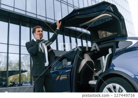 Talking by phone. Businessman is standing near his car outdoors 127449716