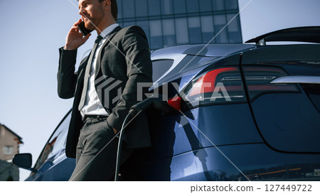 Business call, talking by phone. Man is standing near his electric car outdoors 127449722