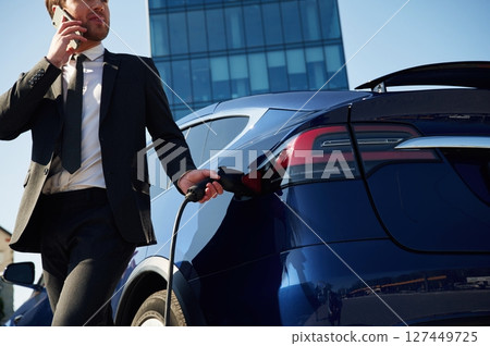 Business call, talking by phone. Man is standing near his electric car outdoors 127449725