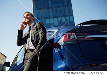 Business call, talking by phone. Man is standing near his electric car outdoors 127449726