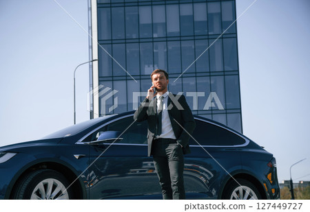 Talking by phone. Businessman is standing near his car outdoors 127449727