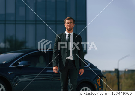 Serious facial expression. Businessman is standing near his electric car outdoors 127449760