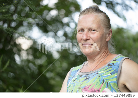 Portrait of an elderly fair-haired woman of normal appearance against a background of greenery. Portrait of an elderly fair-haired woman of normal appearance against a background of greenery. 127449899