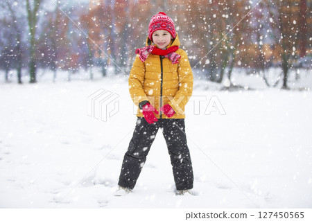 Child in winter. The boy plays on the street against the background of snow. 127450565