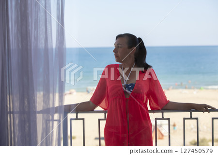 A middle-aged woman stands on a balcony overlooking the sea. A middle-aged woman stands on a balcony overlooking the sea. 127450579