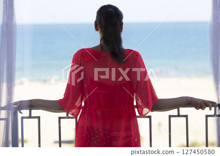 A middle-aged woman stands on a balcony overlooking the sea. A middle-aged woman stands on a balcony overlooking the sea. 127450580