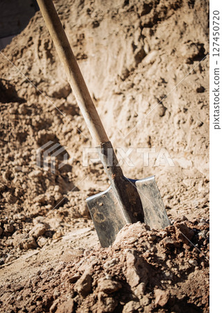 Shovel resting in freshly dug soil at a construction site in the afternoon sun 127450720