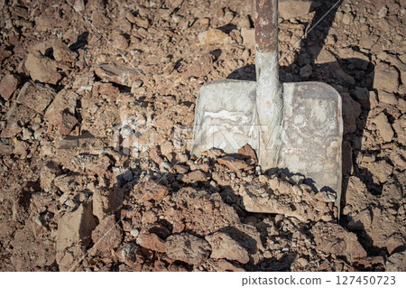 Groundbreaking work with a shovel in dry earth at a construction site during daytime Groundbreaking work with a shovel in dry earth at a construction site during daytime 127450723