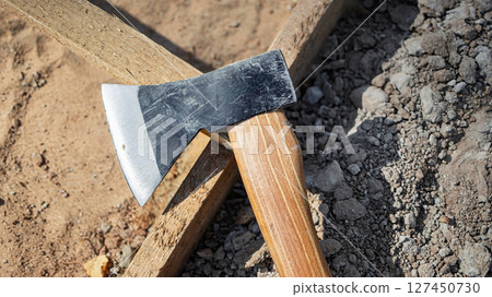 Close-up of an axe resting on a wooden log near gravel and dirt during a construction activity Close-up of an axe resting on a wooden log near gravel and dirt during a construction activity 127450730