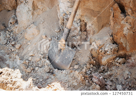 Shovel resting in a pile of dirt at a construction site in midday sun near a developing area 127450731