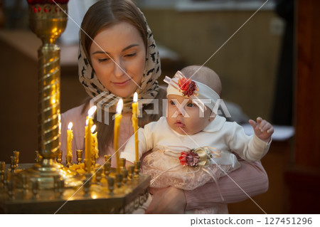 Mother and child in a church by candlelight. Woman with a baby in the temple. 127451296