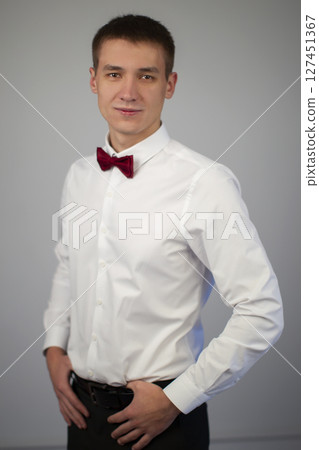 Classic portrait of a young man on a gray background. A guy of about twenty in a white shirt and bow tie. 127451367