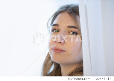 Close-up of the face of a young girl peeping out of the curtains. Close-up of the face of a young girl peeping out of the curtains. 127451412