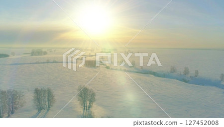 Aerial view of cold winter landscape arctic field, trees covered with frost snow, ice river and sun rays over horizon. Extreme low temperature weather. 127452008