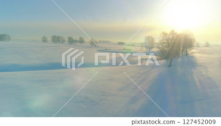 Aerial view of cold winter landscape arctic field, trees covered with frost snow, ice river and sun rays over horizon. Extreme low temperature weather. 127452009